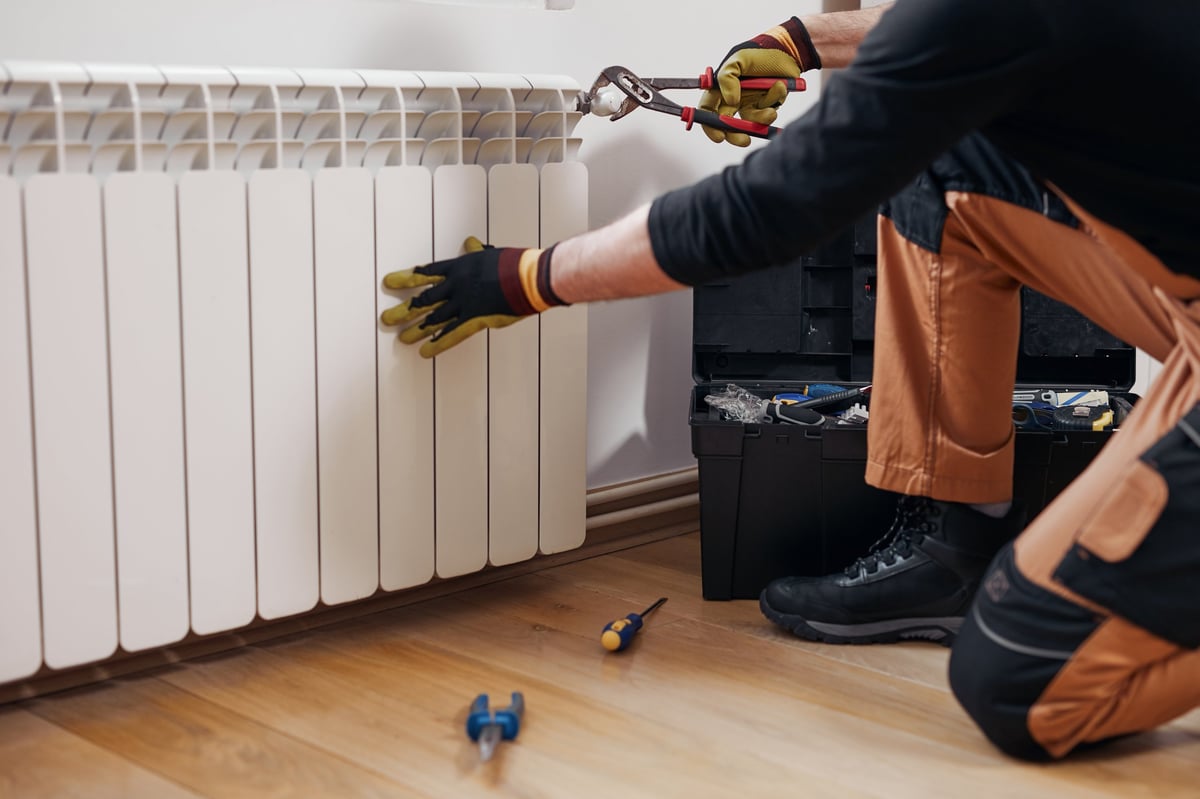 Heating engineer checking a radiator valve while one radiator stays cold in a UK home